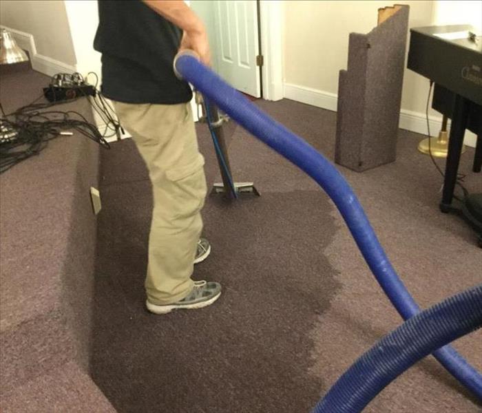 Man's feet and extraction hose and wand extracting water from a carpet
