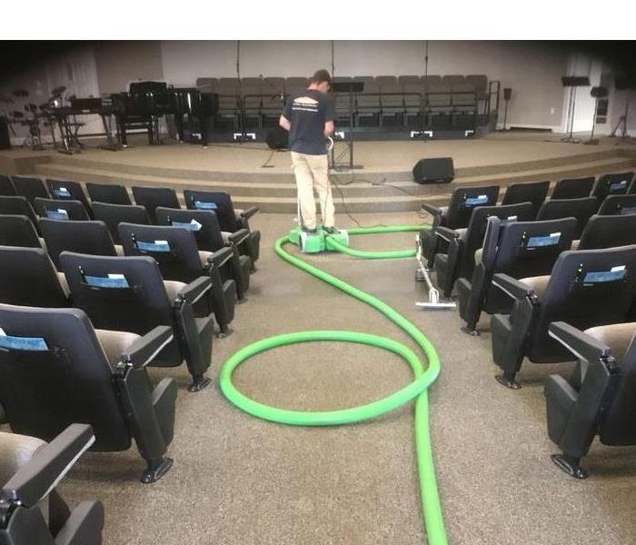 Church sanctuary with stage and a man riding a green piece of equipment extracting water from the carpet