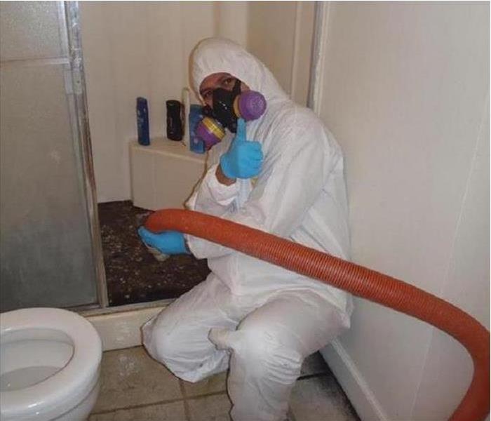 Person in a tyvek suit & respirator with hose extracting sewage from the bottom of a residential shower